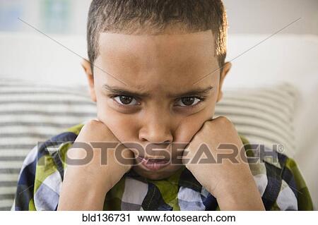 Stock Image - Mixed race boy pouting on sofa. Fotosearch