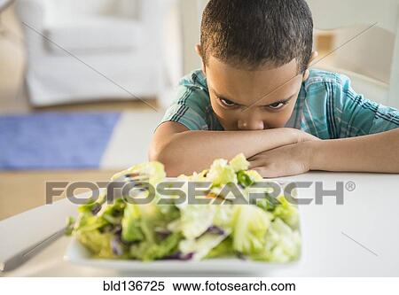Stock Photography - Mixed race boy refusing to eat salad. Fotosearch