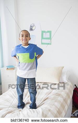 Stock Image - Mixed race boy standing on bed. Fotosearch