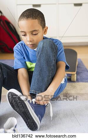 Stock Image - Mixed race boy tying his shoelaces. Fotosearch
