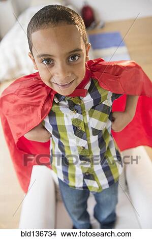 Picture - Mixed race boy wearing cape on armchair. Fotosearch