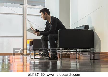 Stock Image - Mixed race businessman reading papers in office lobby. Fotosearch