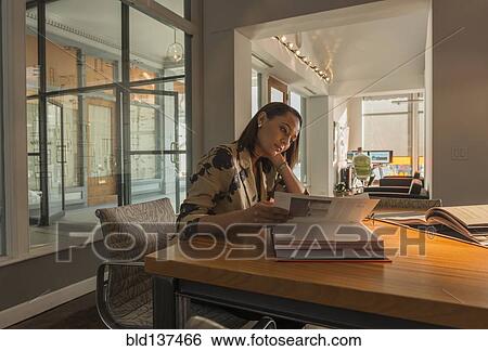 Stock Photograph - Mixed race businesswoman reading at desk. Fotosearch