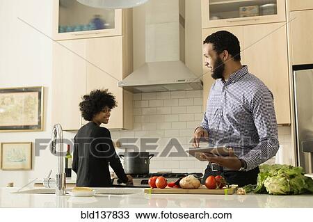 Stock Image - Mixed race couple cooking together in kitchen. Fotosearch