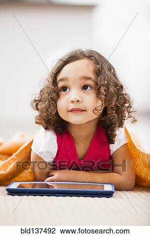Stock Image - Mixed race girl using tablet computer on living room floor. Fotosearch