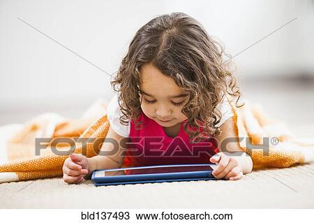 Stock Image - Mixed race girl using tablet computer on living room floor. Fotosearch