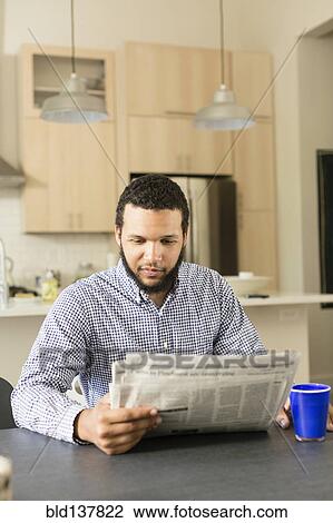 Stock Image - Mixed race man reading newspaper at breakfast table. Fotosearch