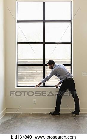 Stock Image - Mixed race realtor measuring window in new house. Fotosearch