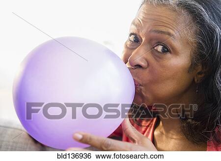 Mixed race woman blowing balloon on sofa View Large Photo Image Stock Photograph - Mixed race woman blowing balloon on sofa. Fotosearch