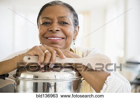 Stock Image - Mixed race woman cooking in kitchen. Fotosearch