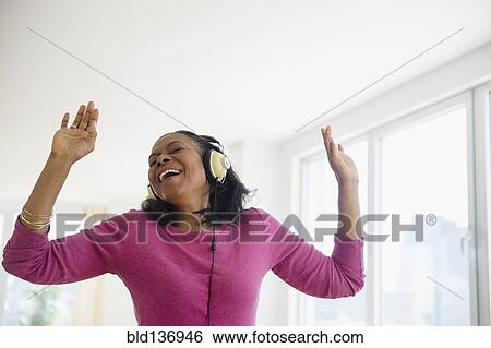 Stock Photograph - Mixed race woman listening to headphones in living room. Fotosearch