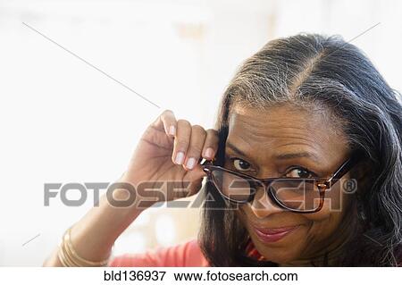Stock Photo - Mixed race woman peering over glasses. Fotosearch