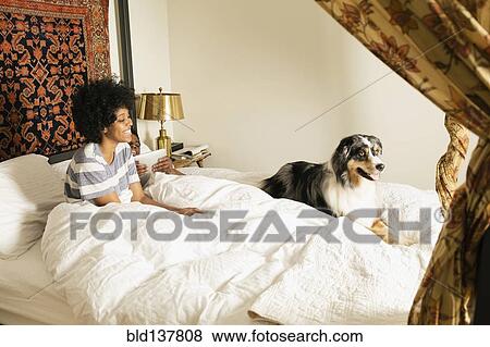 Stock Photo - Mixed race woman sitting with dog in bed. Fotosearch