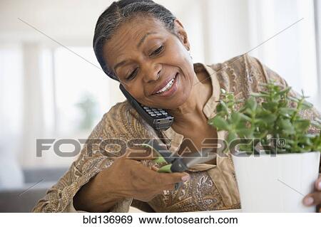 Stock Photo - Mixed race woman trimming plant and talking on phone. Fotosearch