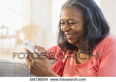 Mixed race woman using cell phone on sofa View Large Photo Image Picture - Mixed race woman using cell phone on sofa. Fotosearch
