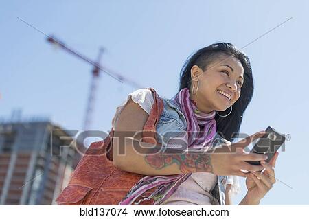 Mixed race woman using cell phone under blue sky View Large Photo Image Picture - Mixed race woman using cell phone under blue sky. Fotosearch