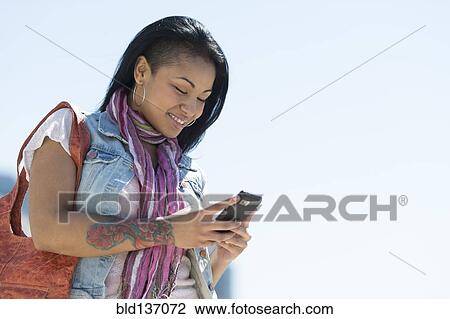 Stock Image - Mixed race woman using cell phone under blue sky. Fotosearch