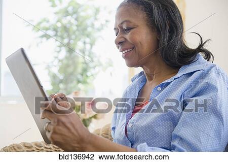 Stock Image - Mixed race woman using tablet computer on sofa. Fotosearch