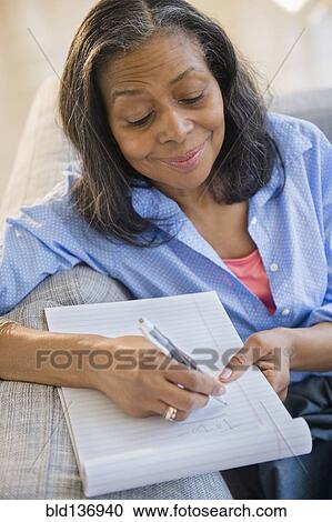 Stock Image - Mixed race woman writing notes on sofa. Fotosearch