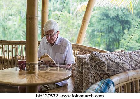 Stock Image - Older Caucasian man reading in bamboo living room. Fotosearch