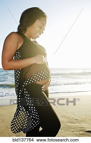 Pregnant woman holding her belly on beach View Large Photo Image Picture - Pregnant woman holding her belly on beach. Fotosearch