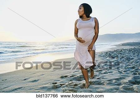 Stock Photograph - Pregnant woman holding her belly on beach. Fotosearch