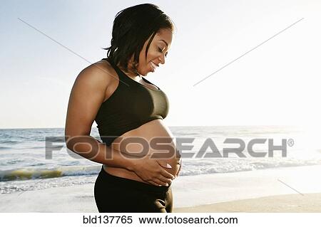 Stock Photography - Pregnant woman holding her belly on beach. Fotosearch