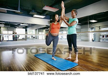 Stock Image - Pregnant woman working with yoga teacher in studio. Fotosearch