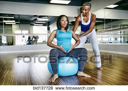 Stock Photo - Pregnant woman working with yoga teacher in studio. Fotosearch