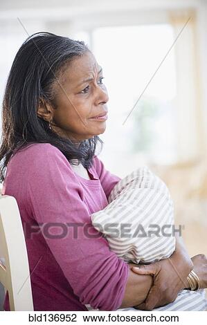 Stock Image - Sad mixed race woman hugging pillow. Fotosearch