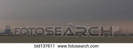 Stock Image - Smoke billowing from distant factory. Fotosearch