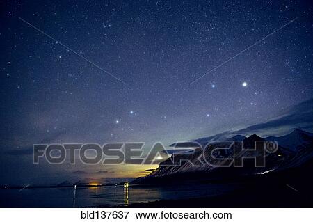 Stock Photo - Starry sky over still ocean in arctic landscape. Fotosearch