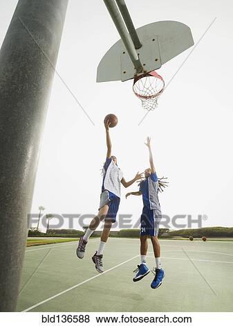Stock Photo - Teenage boys playing basketball on court. Fotosearch