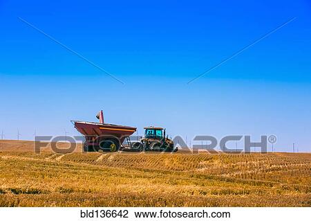 Stock Image - Tractor driving in crop field in rural landscape. Fotosearch