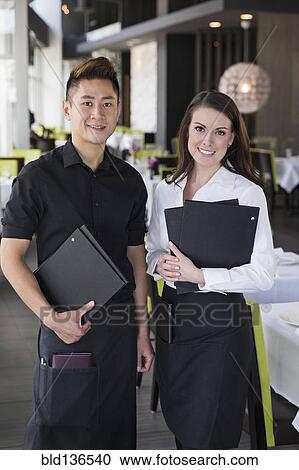 Stock Image - Waiter and waitress smiling together in restaurant. Fotosearch