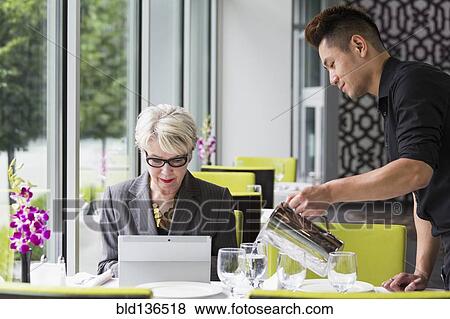 Stock Photo - Waiter pouring water for customer in restaurant. Fotosearch