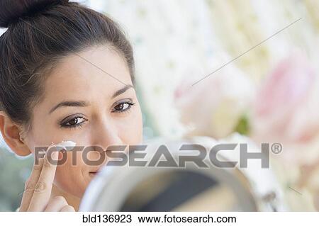 Stock Image - Woman applying moisturizer in mirror. Fotosearch
