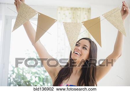 Stock Image - Woman holding bunting flags in living room. Fotosearch