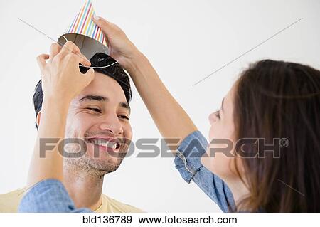 Woman putting party hat on boyfriend View Large Photo Image Stock Photo - Woman putting party hat on boyfriend. Fotosearch