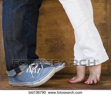 Stock Image - Woman standing on tiptoes to kiss boyfriend. Fotosearch