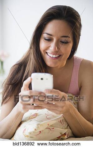 Stock Image - Woman using cell phone on bed. Fotosearch