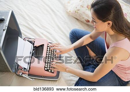 Stock Image - Woman using typewriter on bed. Fotosearch