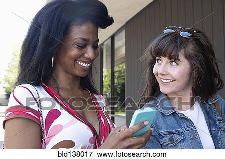 Stock Photo - Women using cell phone together outdoors. Fotosearch