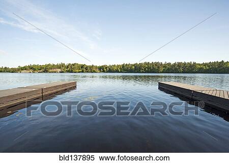 Stock Photography - Wooden docks over still river in rural landscape. Fotosearch