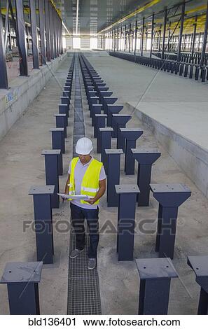 Stock Image - Worker reading blueprints in warehouse. Fotosearch