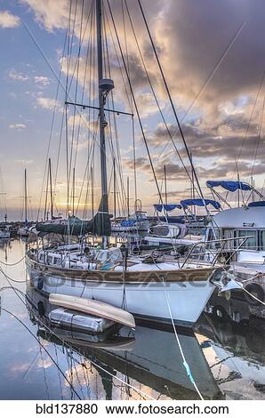 Stock Image - Yacht and cloudy sky reflected in urban harbor. Fotosearch