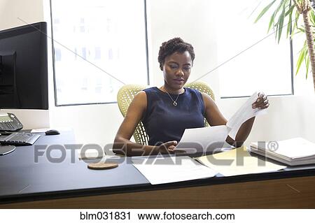 Stock Image - African American businesswoman reading at desk. Fotosearch