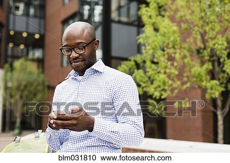 Stock Image - Black man using cell phone in city. Fotosearch
