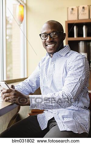 Stock Image - Black man using cell phone in coffee shop. Fotosearch