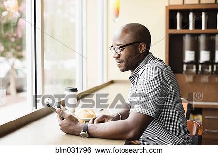 Stock Photograph - Black man using digital tablet in coffee shop. Fotosearch